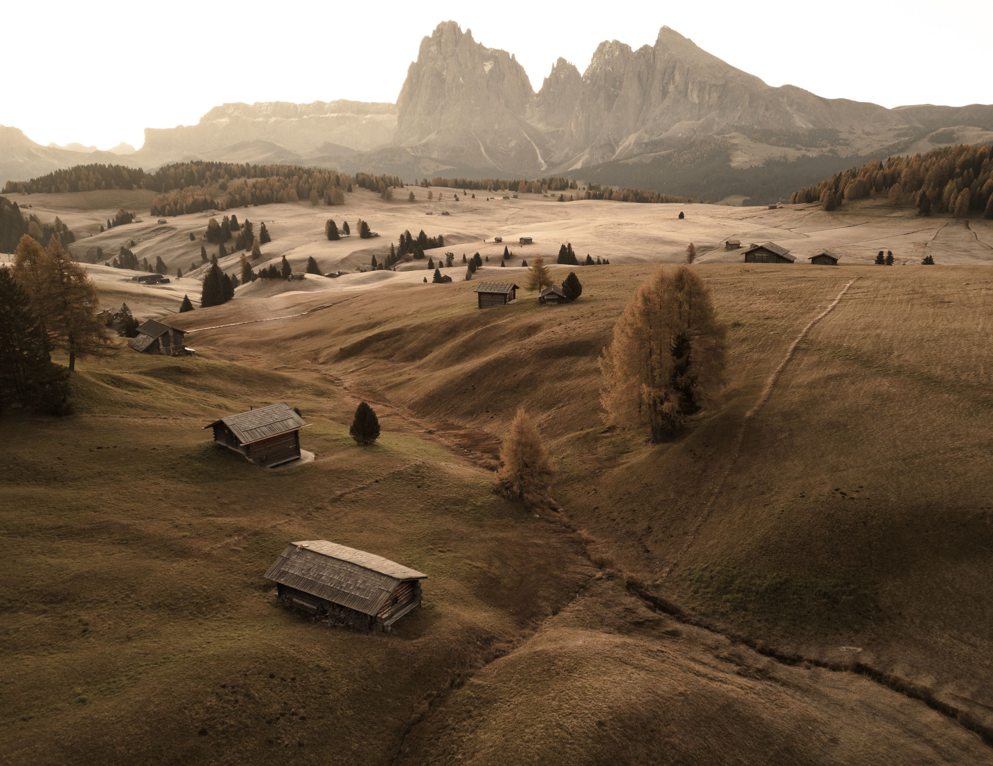A tranquil autumn scene in the Dolomites with scattered rustic huts and lush fields.