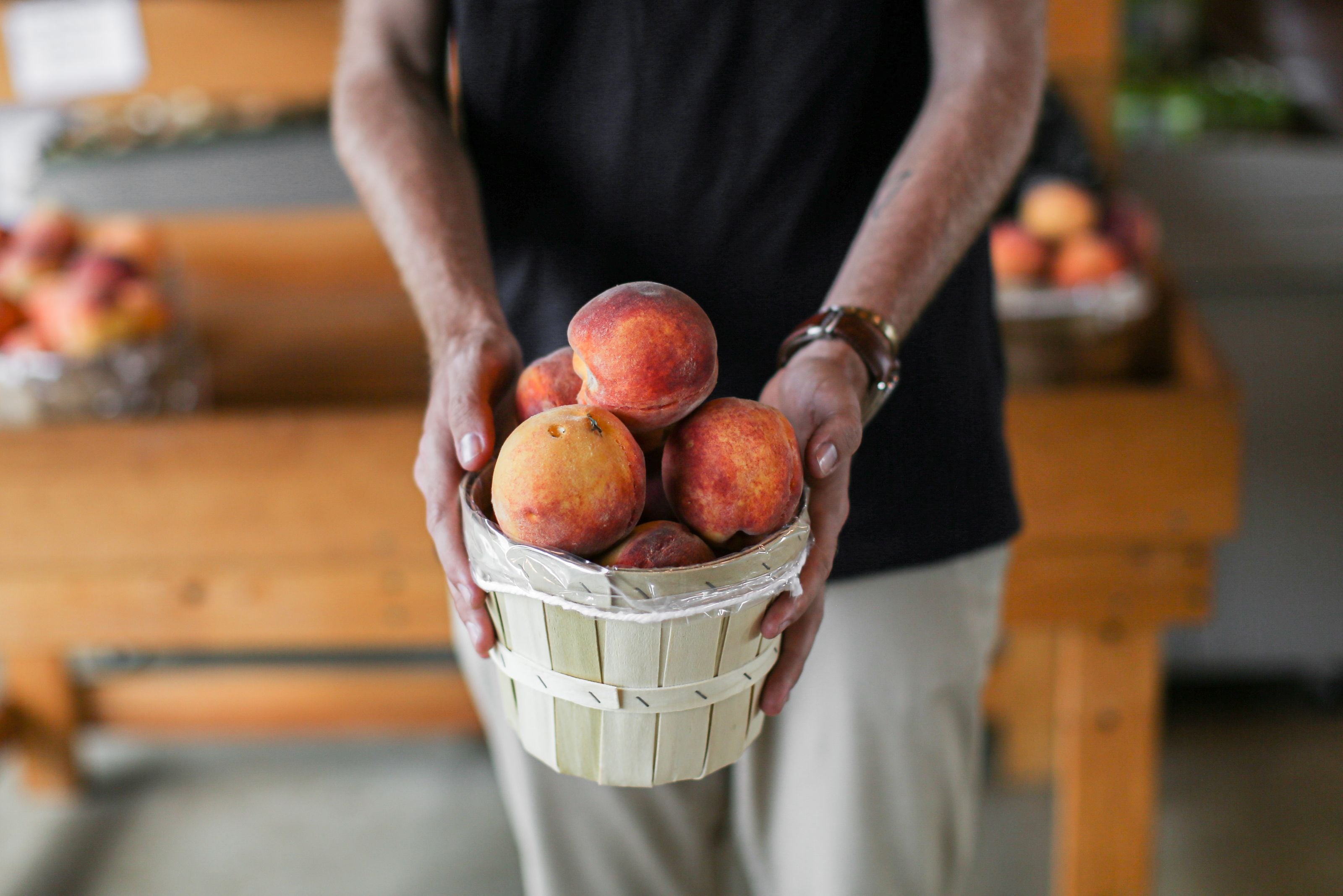 Close-up of hands holding a basket of ripe, juicy peaches at a market stand.