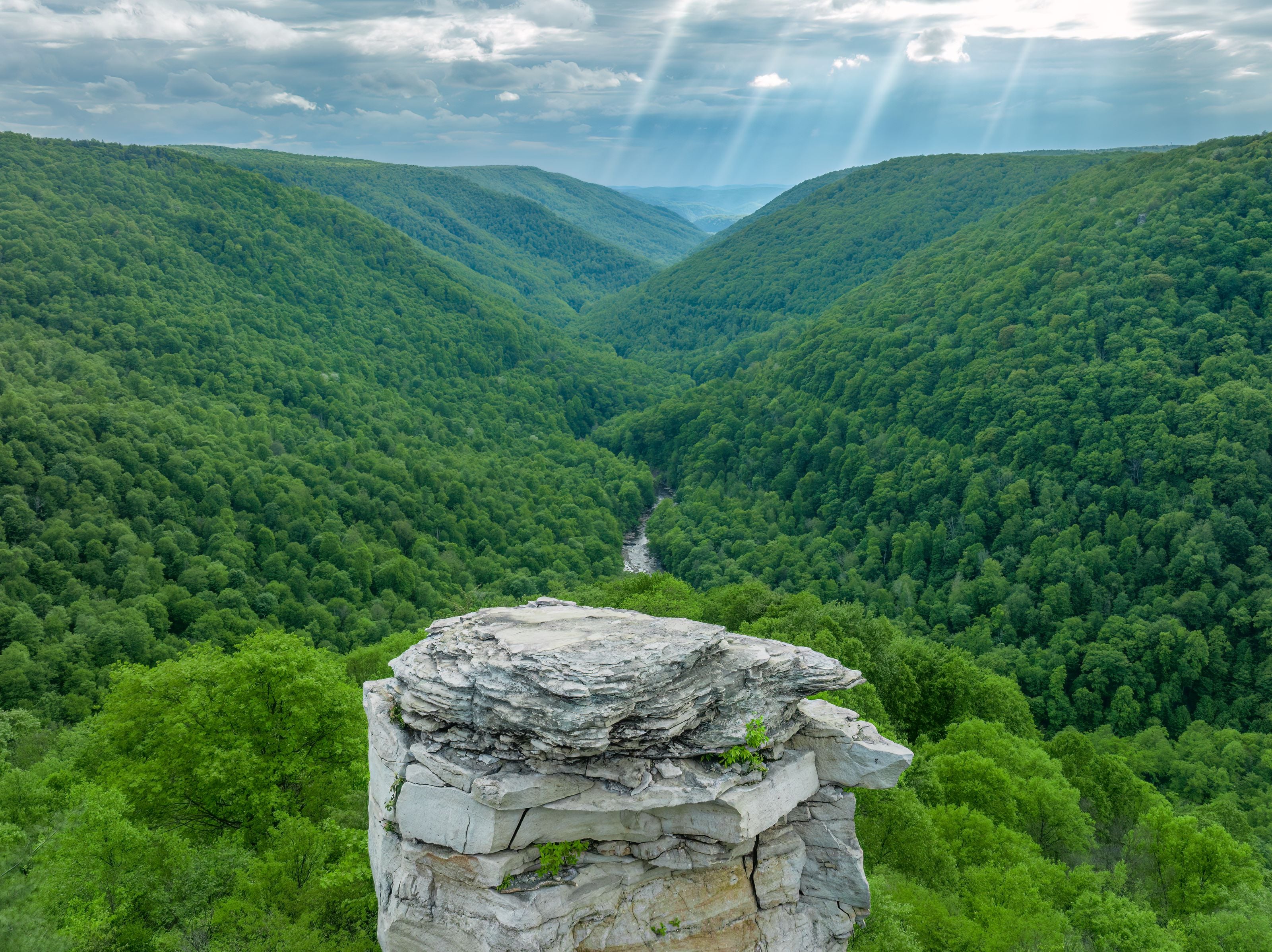 Breathtaking aerial view of a lush green valley in West Virginia, under dramatic sun rays.